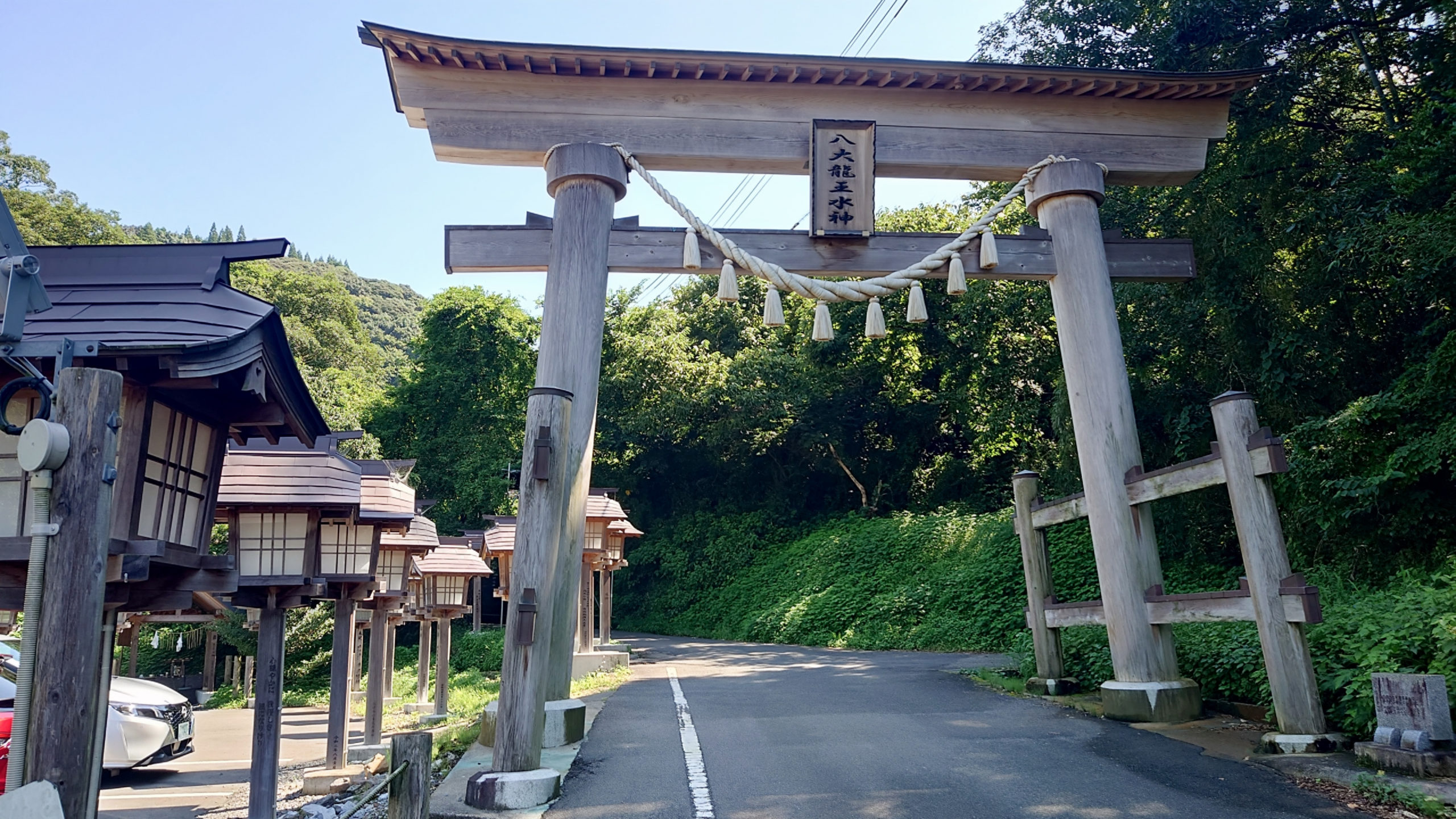 八大龍王水神の参道入口に立つ木製の大鳥居と並ぶ灯籠

